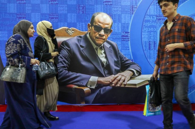 photo d'un poster repr&eacute;sentant l'&eacute;crivain Naguib Mahfouz assis. des personnes passent devant ce poster