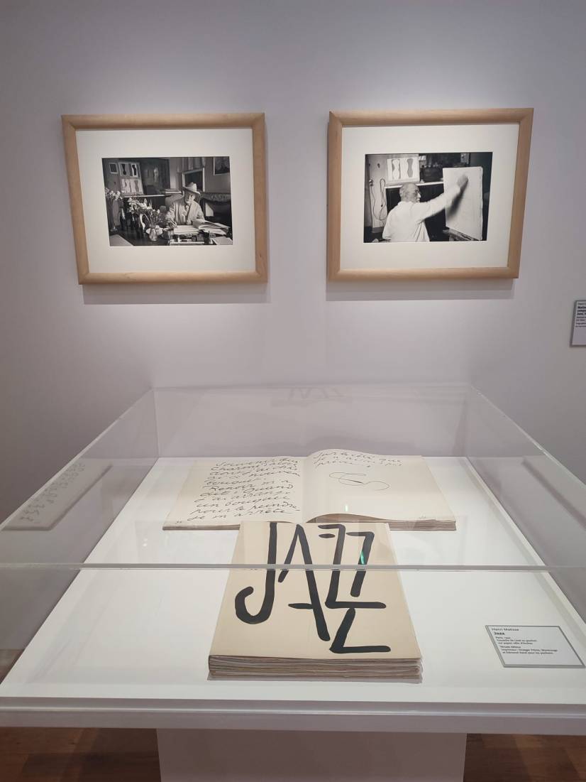 Sur l'image, on découvre une page de l'ouvrage Jazz, l'une des œuvres emblématiques de Matisse, dont un exemplaire est posée à plat dans une vitrine. Sur le mur à l'arrière-plan, deux photographies sont exposées. Elles  montrent Matisse en train de travailler.