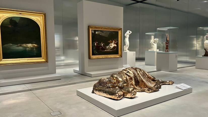 Vue de la Galerie du temps : la sculpture contemporaine dorée de Zanele Muholi est présentée devant deux peintures du 19e siècle