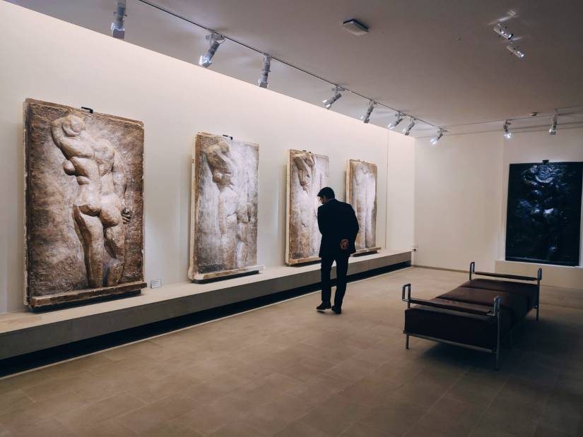 Dans une salle de musée, sont présentée 4 sculptures en haut relief représentant assez schématiquement la même femme nue de dos. Dans cette salle, un homme observe l'une de ces sculptures.