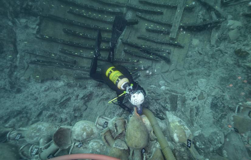 Un fouilleur sous-marin &eacute;quip&eacute; de sa bouteille et d'un casque, &eacute;tiquette des amphores pos&eacute;es en grand nombre sur le fond.