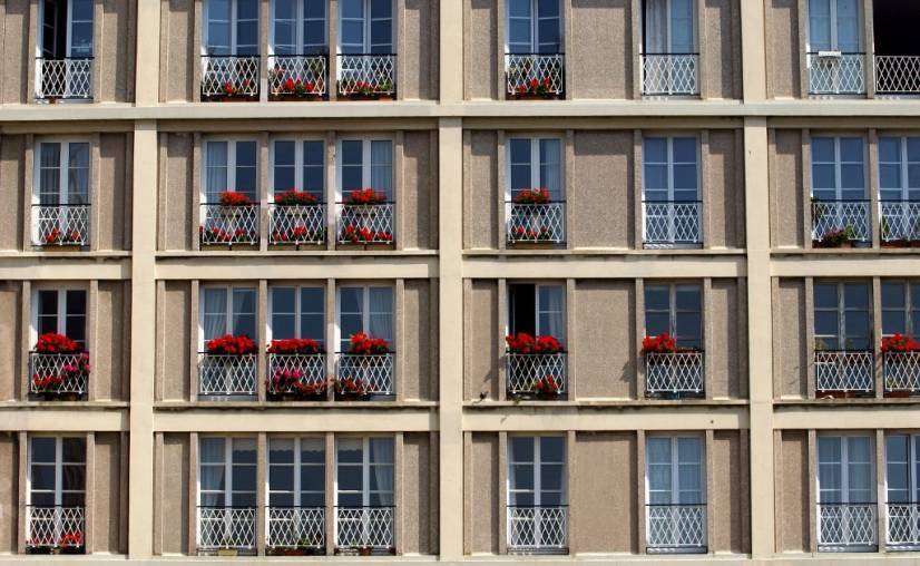photo d'un immeuble gris des années 60 avec des fleurs rouges au bord des fenêtres