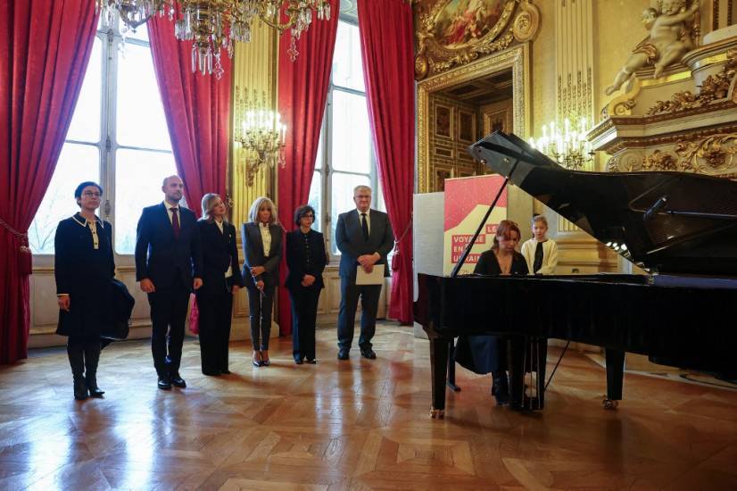 photo de six personnes debout à côté d'une pianiste en train de jouer dans un salon richement décoré