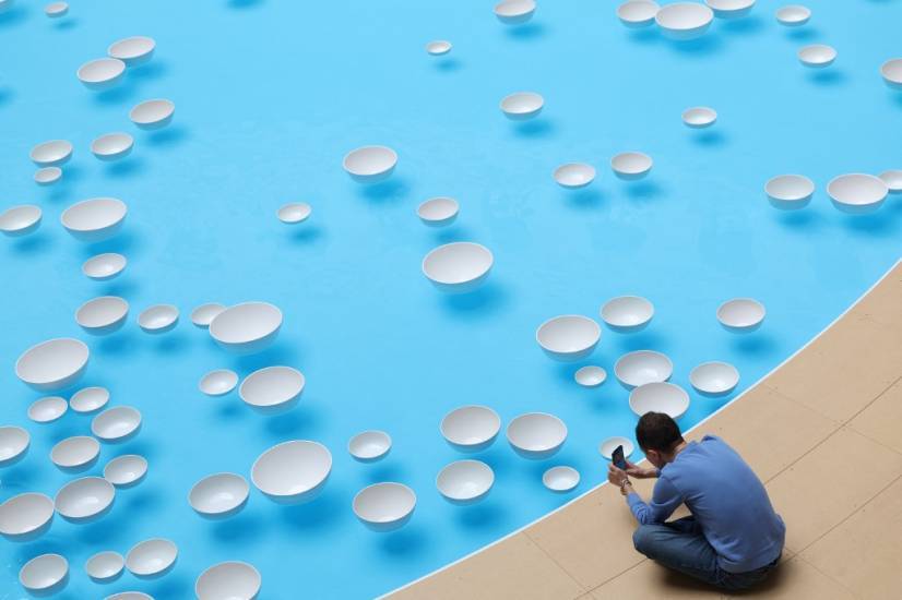 photo prise d'en haut d'un bassin avec des gouttes blanches flottant à la surface. Au bord du bassin, un homme assis prend une photo