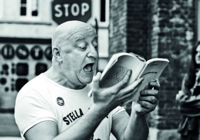 PHOTO 3 : Un homme lit un livre à voix haute avec une expression intense sur le visage. La photographie est en noir et blanc.