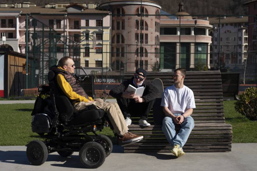 Une personne en fauteuil roulant aux c&ocirc;t&eacute;s de deux personnes valides assises sur un banc