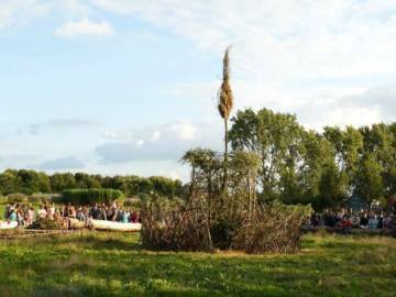 PHOTO 3 : Un grand espace extérieur où une foule de personnes est rassemblée.  Au centre de l'image se trouve une grande structure en branches entrelacées.