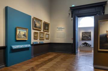 PHOTO 3 : Plusieurs tableaux encadrés sont accrochés aux murs d’une salle d’exposition.