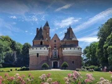 PHOTO 6 : Le château de Rambures, en brique rouges, entouré de son parc. Devant le château, une pelouse verte est bordée de massifs de fleurs roses. De grands arbres entourent la propriété.