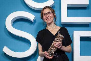 photo d'une femme en robe noire tenant un cesar &agrave; la main et posant devant un d&eacute;cor des cesar avec des lettres blanches sur fond bleu