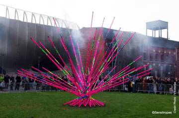Photo 2 : Une installation de perches d’athlétisme de couleur rose est disposée comme un bouquet. En arrière-plan, des individus sont dans un parc. Une barrière les empêche de s’approcher trop près de l’installation.