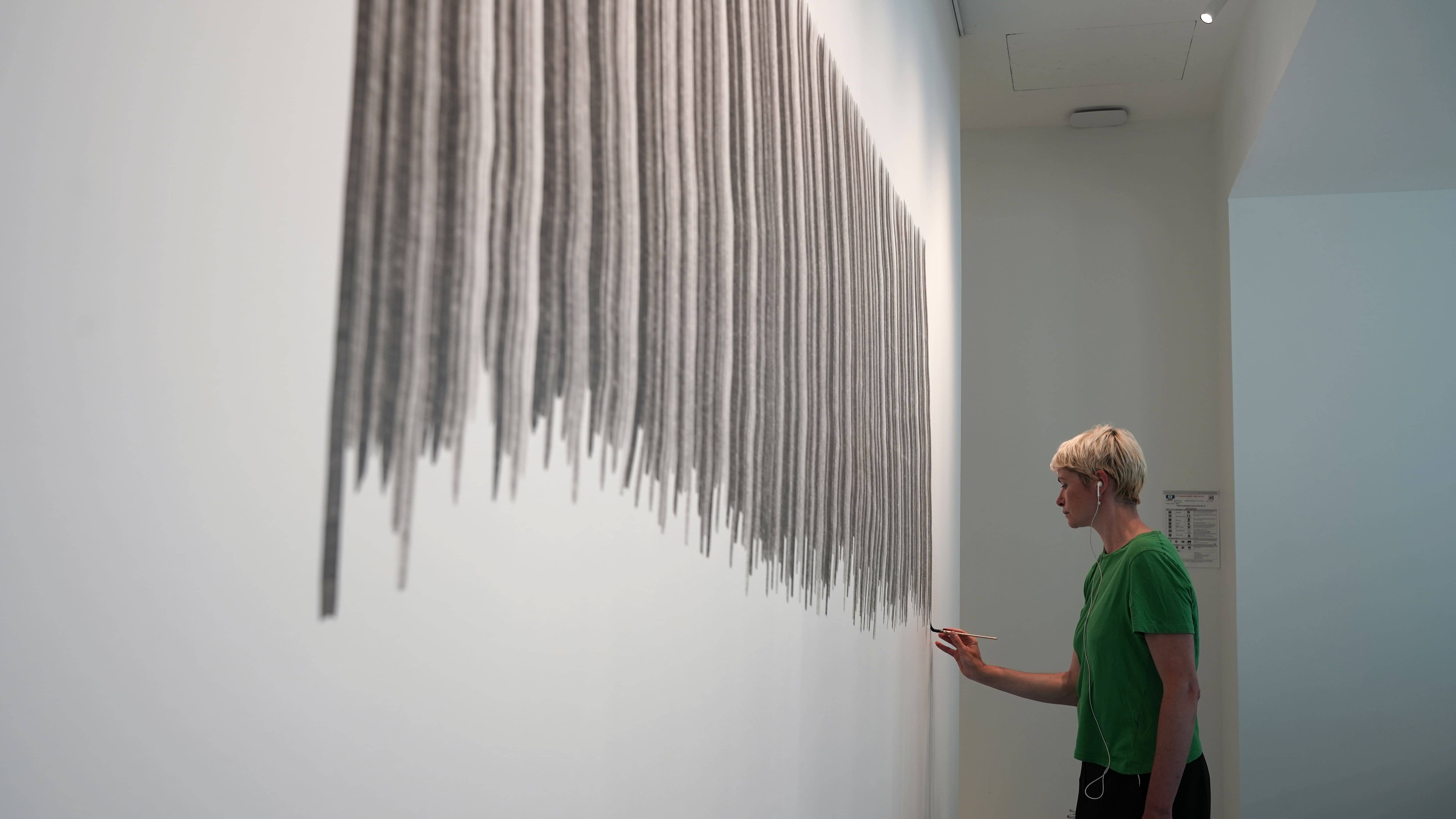 artiste vue de profil traçant des lignes sur un mur blanc