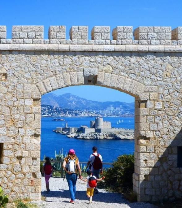 photo du chateau d'if avec des promeneurs qui passent sous une arche et la mer en arrière plan