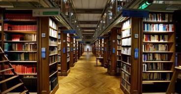 photo d'une bibliothèque prise en soirée avec une allée centrale et des rayons de livre de chaque côté.