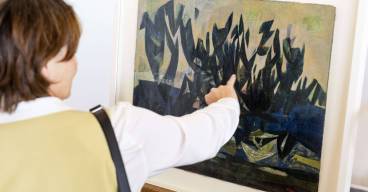 photo d'une femme de dos en train de regarder et de montrer un tableau