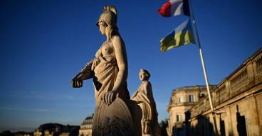 photo prise depuis le toit d'un opéra avec deux statues au premier plan, les drapeaux ukrainiens et français au second plan sous un ciel bleu