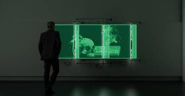 photo d'un écran vert avec un crâne et d'une personne de dos, dans le noir, en train de le regarder