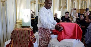 photo d'un homme debout devant un coffre recouvert d'un tissu rouge en train de le bénir