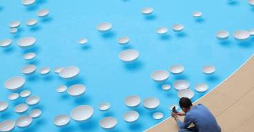photo prise d'en haut d'un bassin avec des gouttes blanches flottant à la surface. Au bord du bassin, un homme assis prend une photo