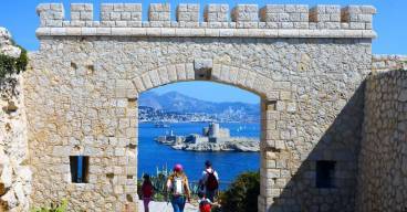 photo du chateau d'if avec des promeneurs qui passent sous une arche et la mer en arrière plan