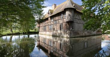 Photo du manoir de Coupesarte en Normandie, maison à colombage au bord d'un plan d'eau avec des arbres