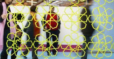 photo d'un mur ajouré avec des motifs jaunes et des personnes floues en arrière plan