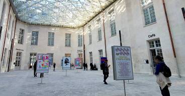photo de la Cité internationale de la langue française à Villers-Cotterêts sous une verrière avec seize affiches exposées et des visiteurs qui les regardent