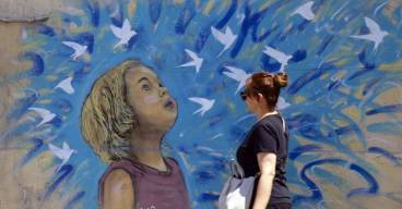 photo d'une femme marchant devant un dessin de street art représentant une jeune fille avec des oiseaux qui s'envolent dans les tons bleus