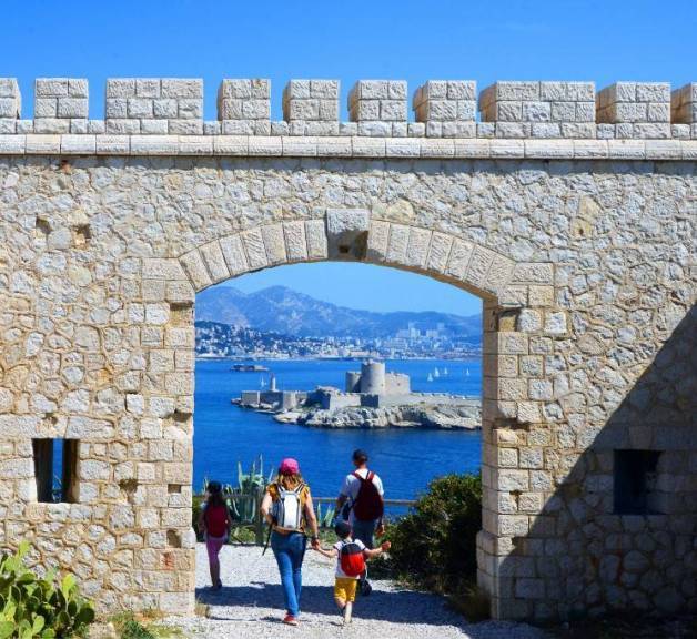 photo du chateau d'if avec des promeneurs qui passent sous une arche et la mer en arrière plan