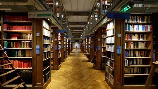 photo d'une bibliothèque prise en soirée avec une allée centrale et des rayons de livre de chaque côté.