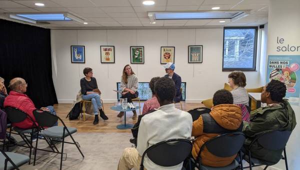 photo avec une petite conférence dans une bibliothèque avec du public de dos et trois intervenants de face assis
