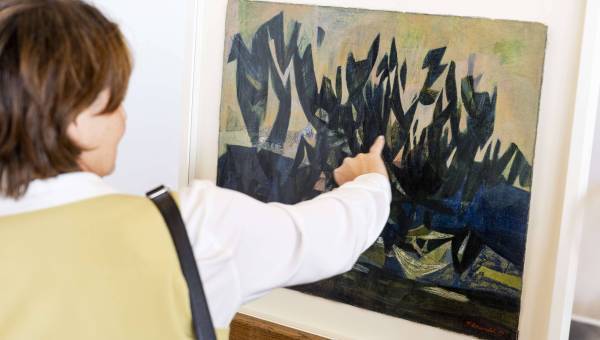 photo d'une femme de dos en train de regarder et de montrer un tableau