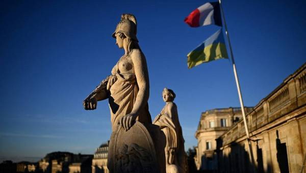 photo prise depuis le toit d'un opéra avec deux statues au premier plan, les drapeaux ukrainiens et français au second plan sous un ciel bleu