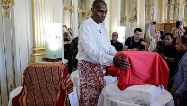 photo d'un homme debout devant un coffre recouvert d'un tissu rouge en train de le bénir