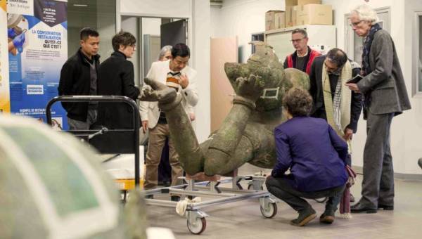 Examen par un groupe de personnes de la statue colossale en bronze du Vishnou couché du Mébon occidental, au laboratoire Arc'Antique
