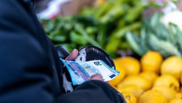 photo d'une personne tenant son porte monnaie avec des billets devant un stand de fruits et légumes