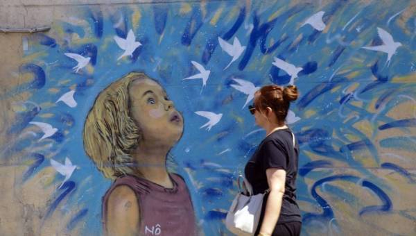 photo d'une femme marchant devant un dessin de street art représentant une jeune fille avec des oiseaux qui s'envolent dans les tons bleus
