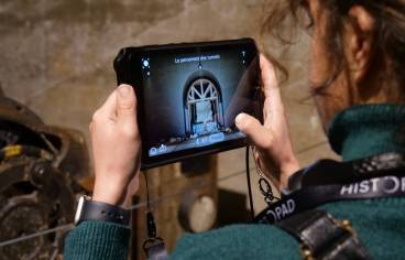 De dos, un visiteur apprend à se servir de l'Histopad, une tablette tactile qui permet une visite immersive de La Coupole