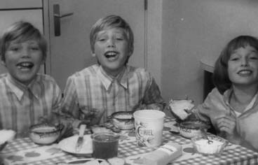 Photo en noir et blanc de trois enfants souriants à table, au petit-déjeuner.