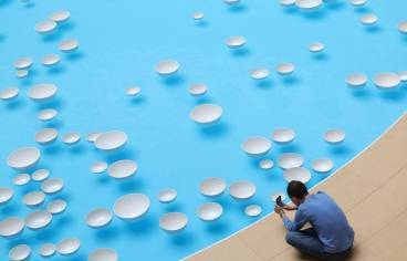 photo prise d'en haut d'un bassin avec des gouttes blanches flottant à la surface. Au bord du bassin, un homme assis prend une photo