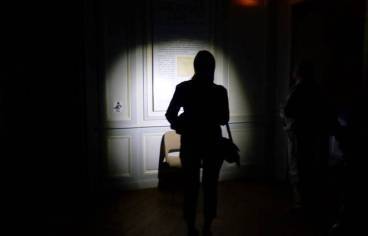 photo d'une femme tenant une lampe torche dans un musée, ambiance sombre avec juste le halo qui éclaire une oeuvre