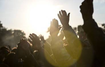 photo prise lors d'un festival en plein air, avec gros plan sur des bras levés en contre jour
