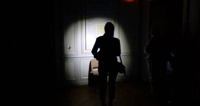 photo d'une femme tenant une lampe torche dans un musée, ambiance sombre avec juste le halo qui éclaire une oeuvre
