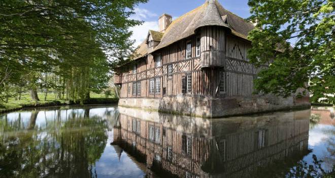 Photo du manoir de Coupesarte en Normandie, maison à colombage au bord d'un plan d'eau avec des arbres