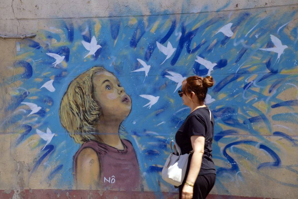 photo d'une femme marchant devant un dessin de street art représentant une jeune fille avec des oiseaux qui s'envolent dans les tons bleus