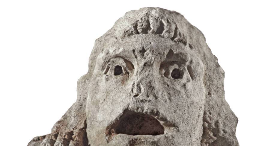 Vue rapprochée d'un acrotère en pierre en forme de masque de théâtre, représentant un adolescent, découvert dans le puits à dromos LX à Glanum.