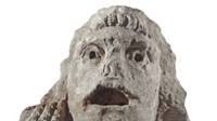 Vue rapprochée d'un acrotère en pierre en forme de masque de théâtre, représentant un adolescent, découvert dans le puits à dromos LX à Glanum.