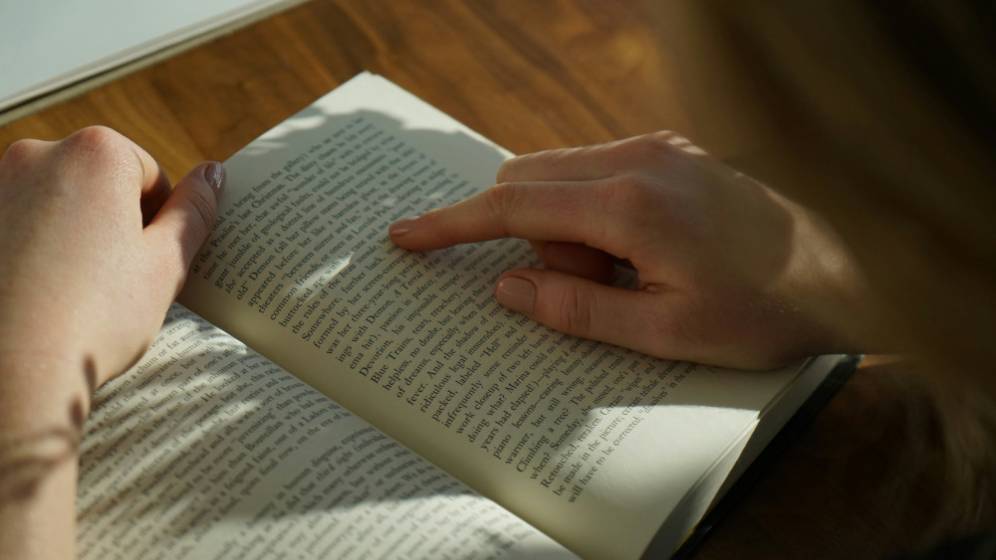 livre ouvert, une main en train de pointer les mots sur la page de droite