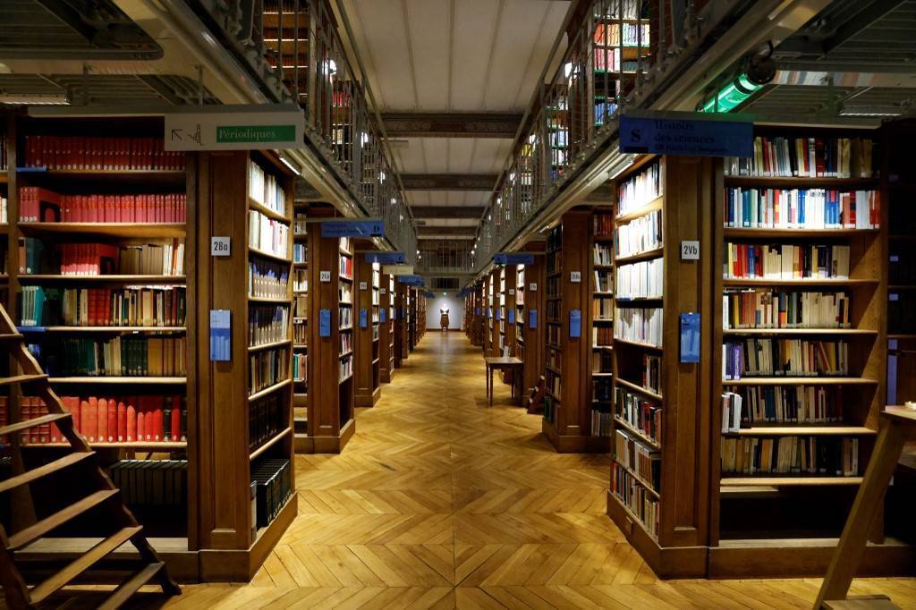 photo d'une bibliothèque prise en soirée avec une allée centrale et des rayons de livre de chaque côté.