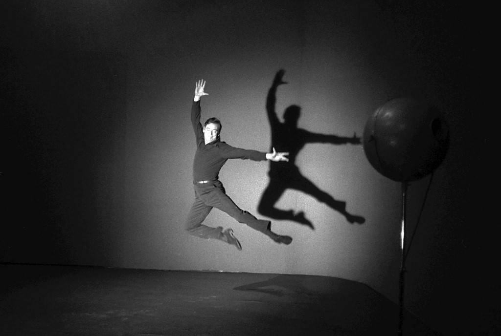 photo en noir et blanc d'un homme qui danse sur scène avec son ombre derrière